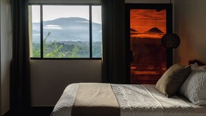 A bedroom with a large window, a bed with a blanket, and a view of a mountain. - Hotel Juayua (Juayua)