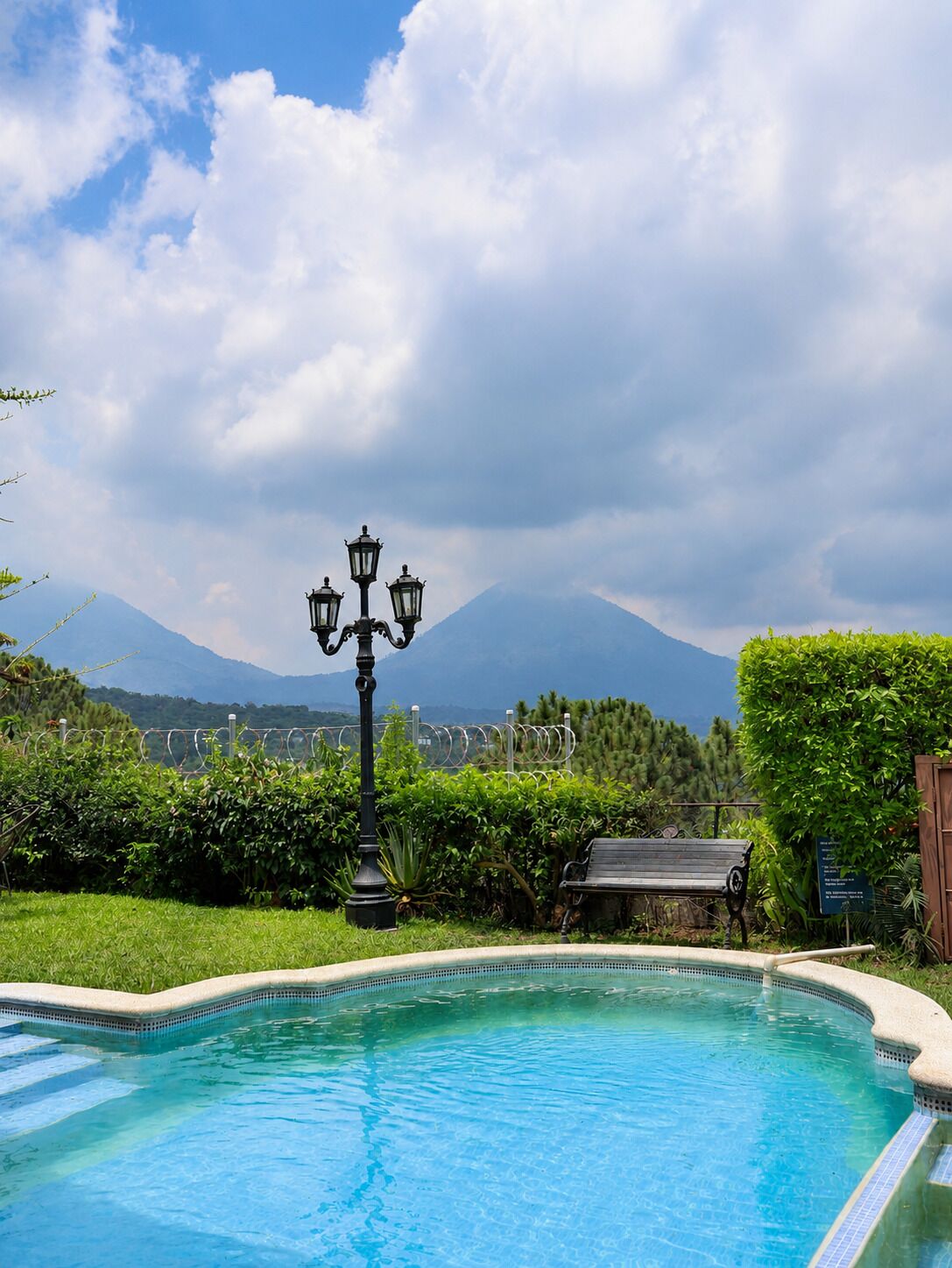 A swimming pool with a mountain view, a bench, and a lamp post.