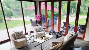 Amplia sala de estar con un gran ventanal corredero que da a un patio exterior con mobiliario y vistas a un lago.