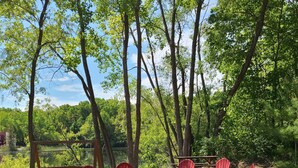 Un camping con sillas Adirondack rojas dispuestas alrededor de un brasero central, rodeado de árboles y suelo arenoso.