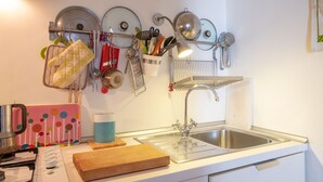 Una cocina con un lavamanos de acero inoxidable, una tabla de cortar de madera, una tetera y varios utensilios colgados en la pared.