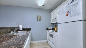 Una cocina con encimeras de granito, armarios blancos, un refrigerador y un microondas.