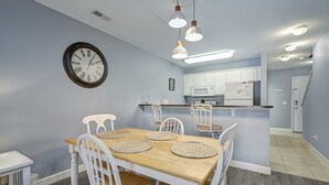 Un comedor con una mesa de madera, sillas blancas y un reloj de pared.