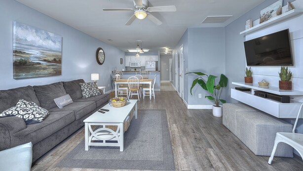 Una sala de estar moderna con un sofá gris, una mesa de centro blanca y una zona de comedor con una mesa y sillas de madera.