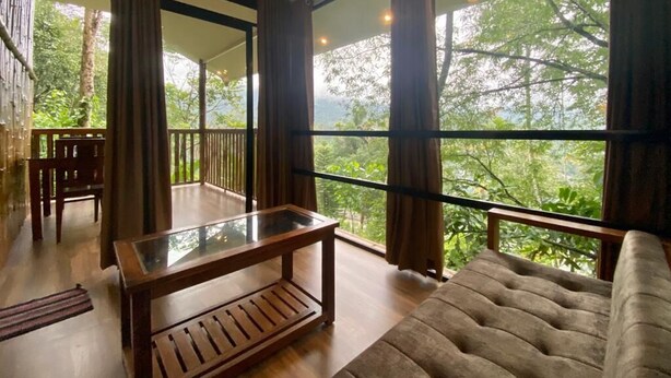 Um quarto espaçoso com uma grande janela, uma mesa de madeira, um sofá confortável e vista para o verde lá fora.