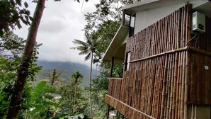 Edifício com paredes de bambu e varanda com vista para uma paisagem montanhosa.