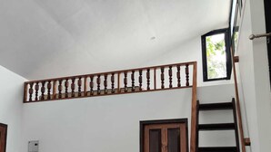 Um quarto com porta de madeira, uma pequena janela, uma escada de madeira e teto branco.