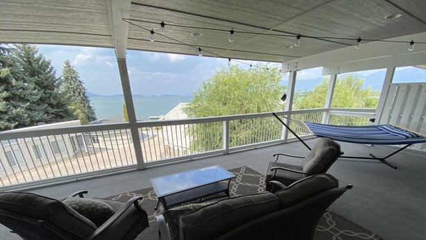 A covered outdoor seating area with a view of the lake, a hammock, and a table. - Lakefront Oasis - Lakefront w/ Views, Private Shared Dock, Wrap Around Deck (Polson)