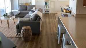 A modern living room with a grey sofa, a coffee table, and a bookshelf. - Lakefront Oasis - Lakefront w/ Views, Private Shared Dock, Wrap Around Deck (Polson)