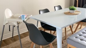 A dining area with a white table, black chairs, a high chair, a potted plant, and a wall-mounted light fixture. - Lakefront Oasis - Lakefront w/ Views, Private Shared Dock, Wrap Around Deck (Polson)