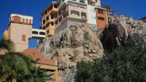 A multi-story hotel built on a rocky cliff with balconies and a mix of beige and white colors. - Luxurious Penthouse Suite on the Ridge or Beachfront side- Playa Grande Resort  (Cabo San Lucas)