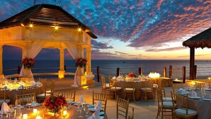 An outdoor dining area with tables set for a meal, overlooking the sea, under a gazebo with a thatched roof. - Luxurious Penthouse Suite on the Ridge or Beachfront side- Playa Grande Resort  (Cabo San Lucas)