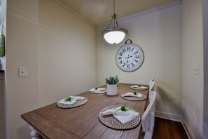 Een eetgedeelte met een houten tafel voor vier personen, een hanglamp en een wandklok.