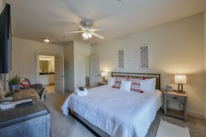 A bedroom with a large bed, bedside tables with lamps, a ceiling fan, and a TV on a stand.