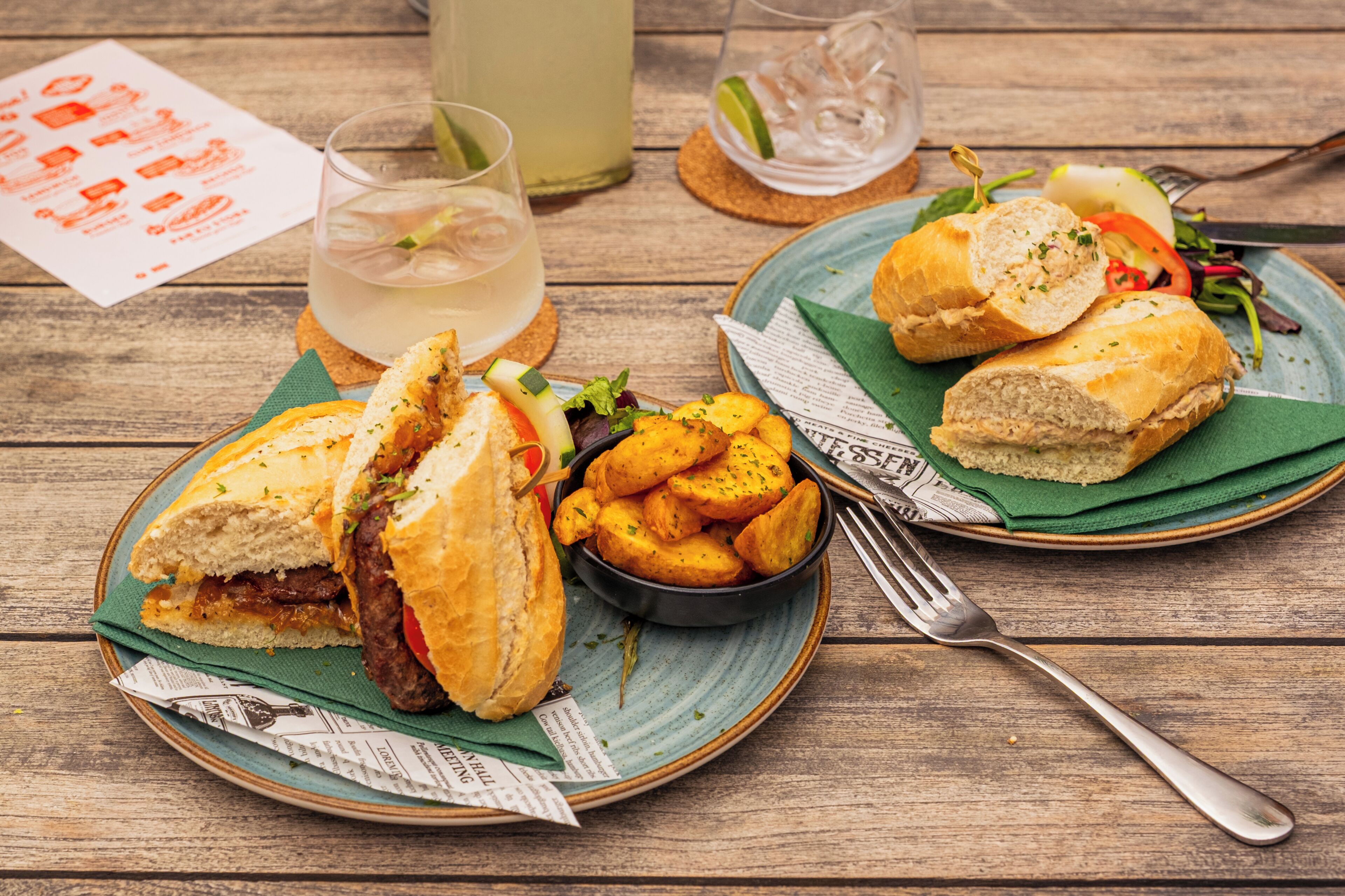 Una comida con sándwiches, papas fritas y una bebida sobre una mesa de madera.