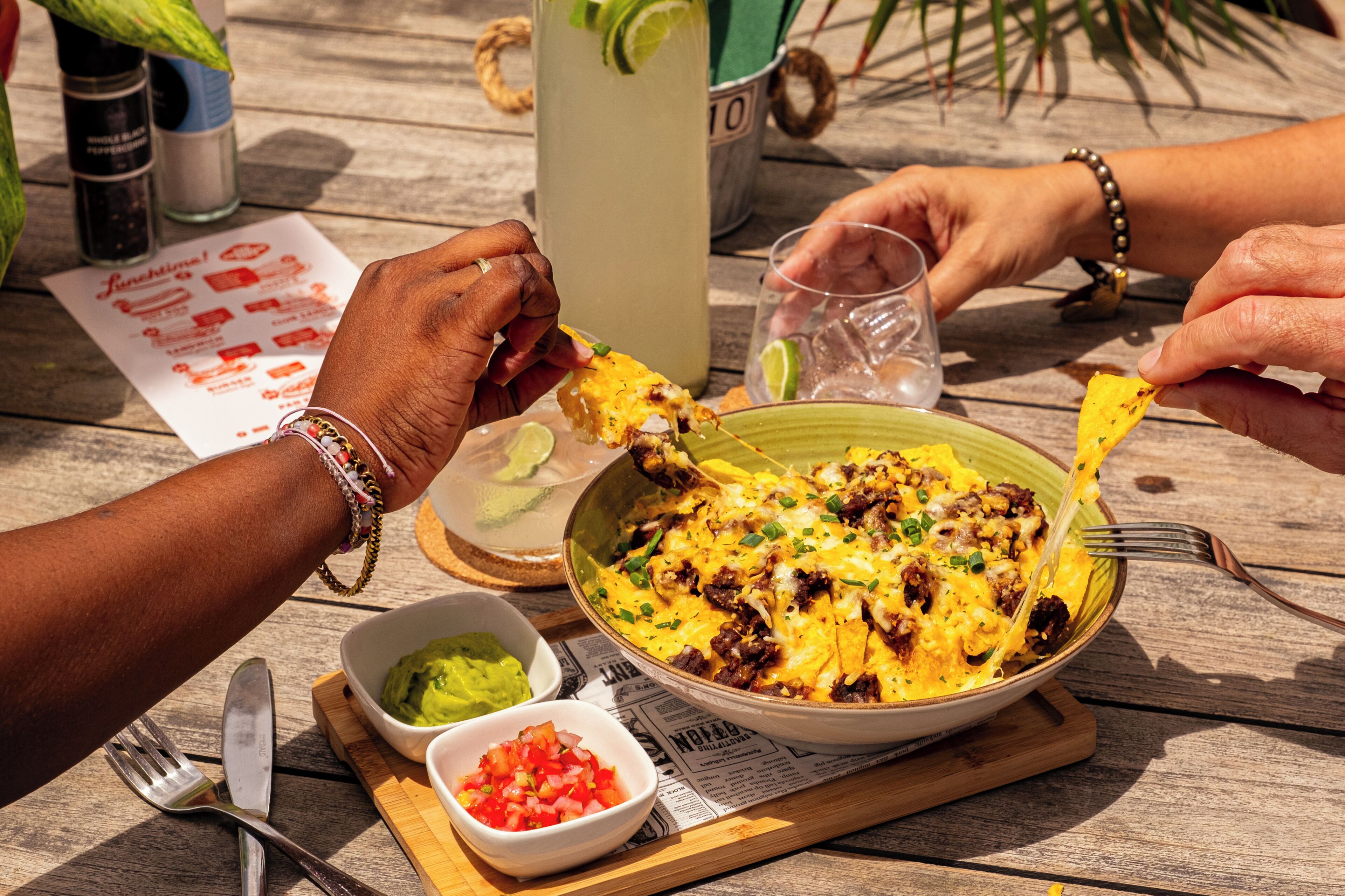 A meal with nachos, guacamole, and salsa on a wooden table.
