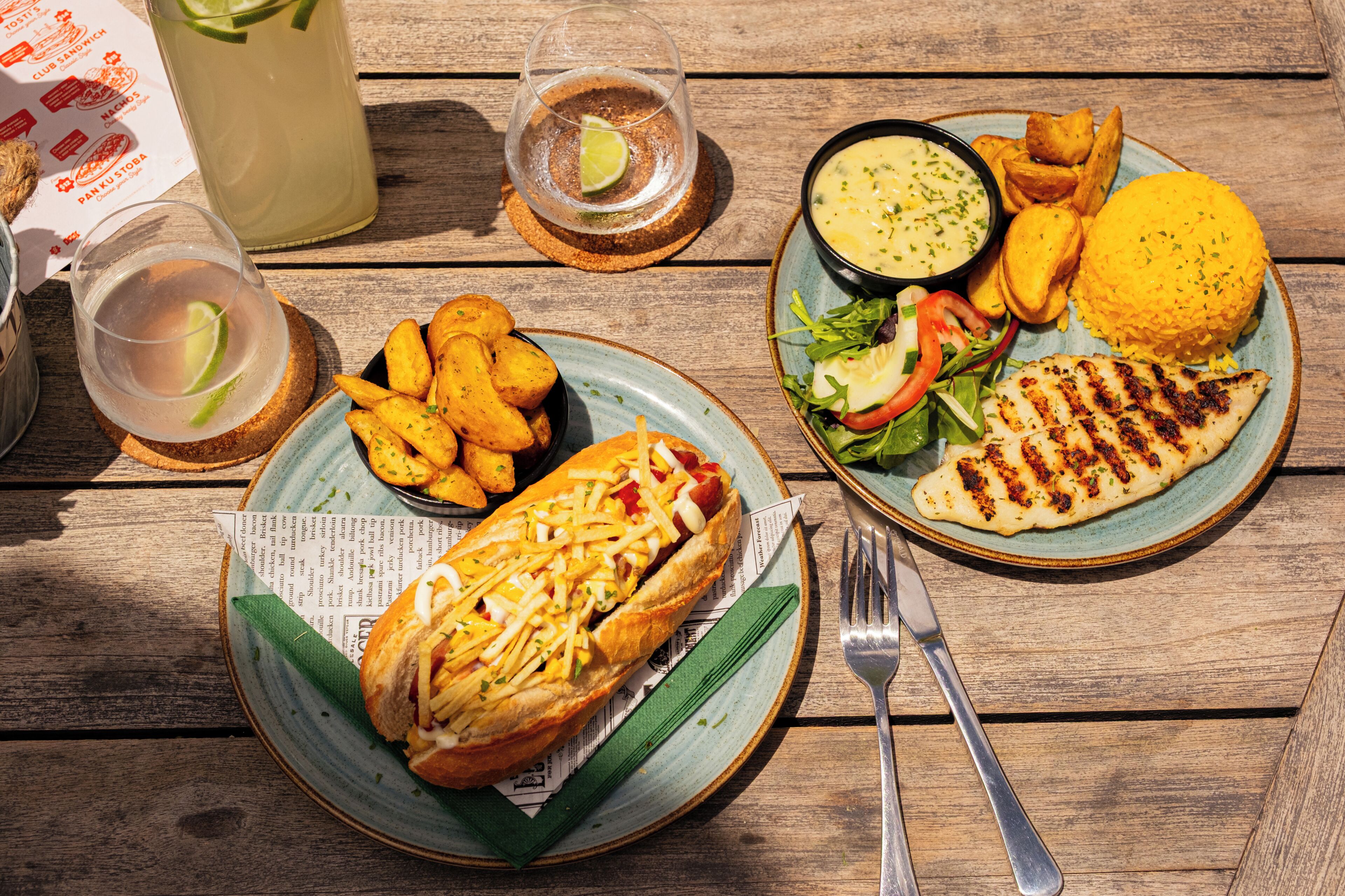 Una comida con un sándwich, papas fritas, una ensalada y algo a la parrilla sobre una mesa de madera.