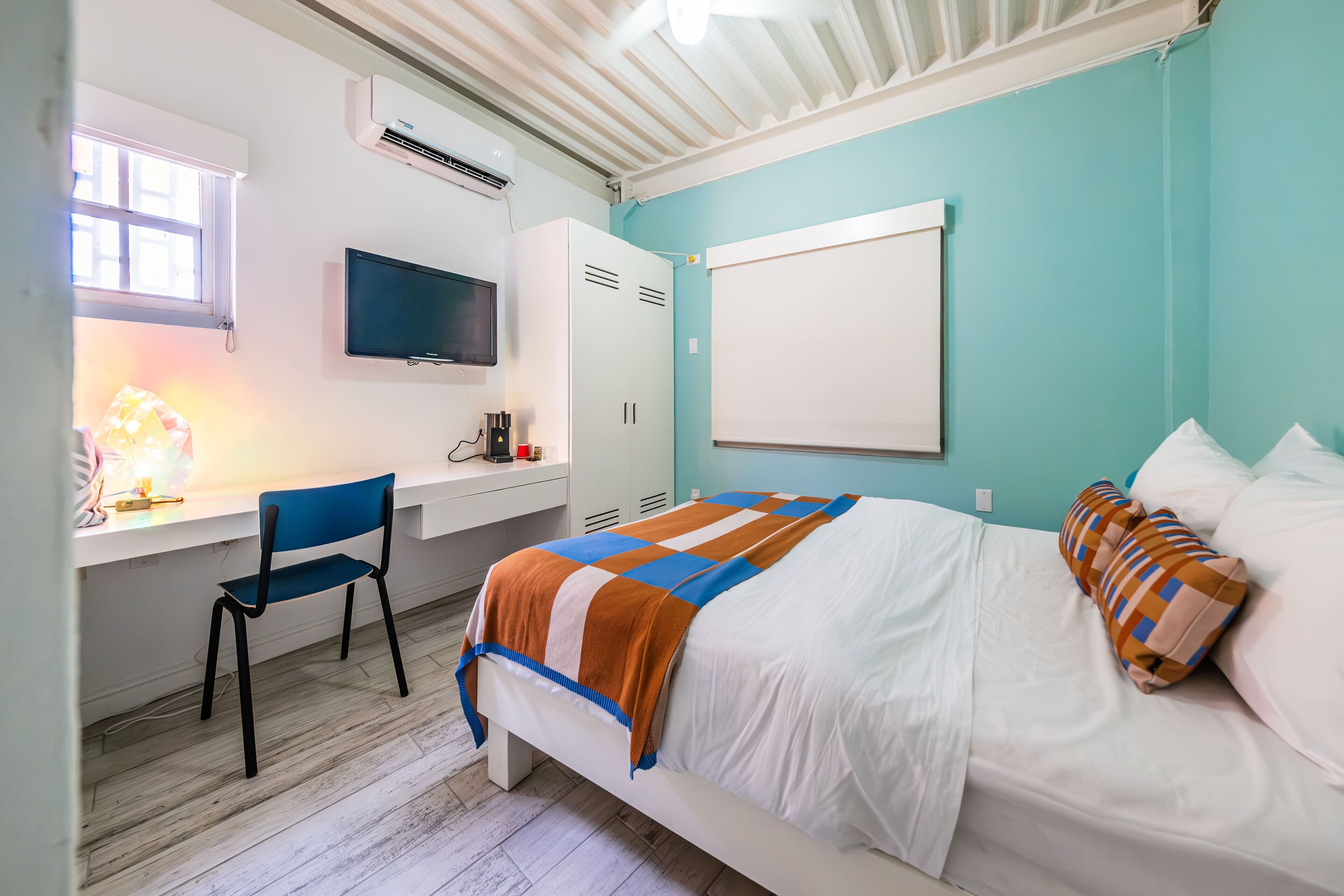 Ein Schlafzimmer mit einem Bett, einem Schreibtisch, einem Stuhl, einem Fernseher und einem Fenster.