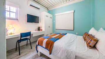 A bedroom with a bed, a desk, a chair, a TV, and a window.