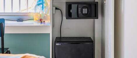 A compact room with a bed, a desk with a lamp, a microwave, and a small black refrigerator.