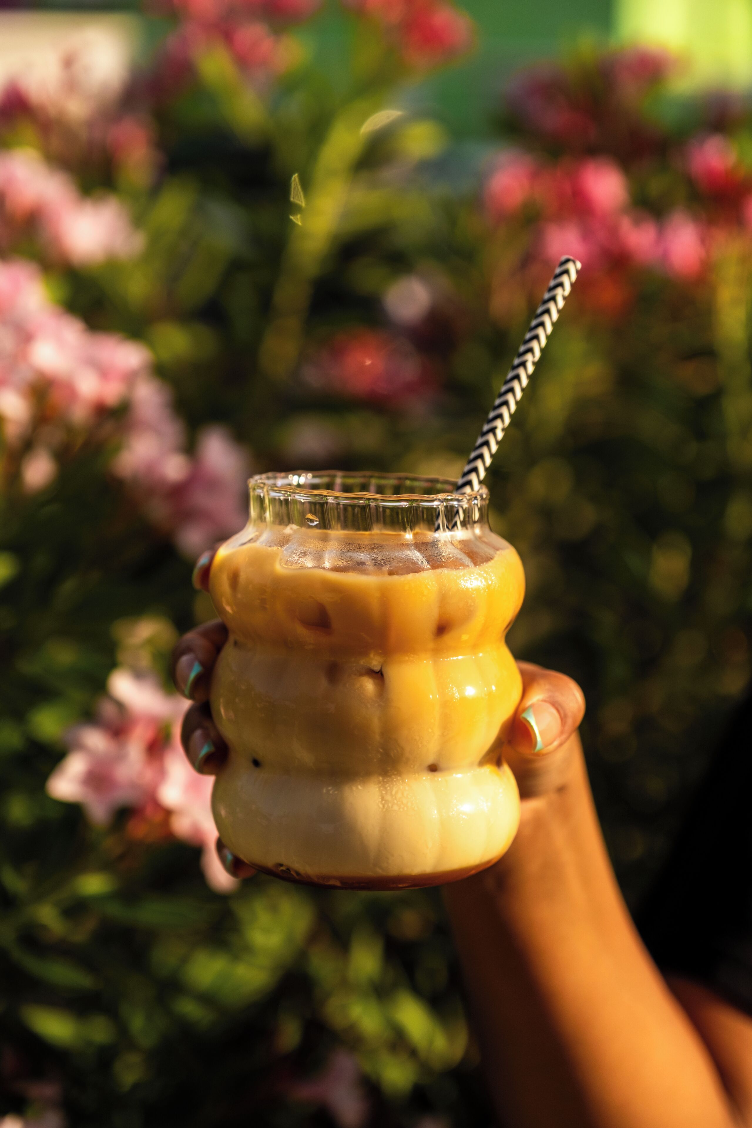 Una mano sosteniendo un vaso con pajita, que contiene una bebida con cubitos de hielo.