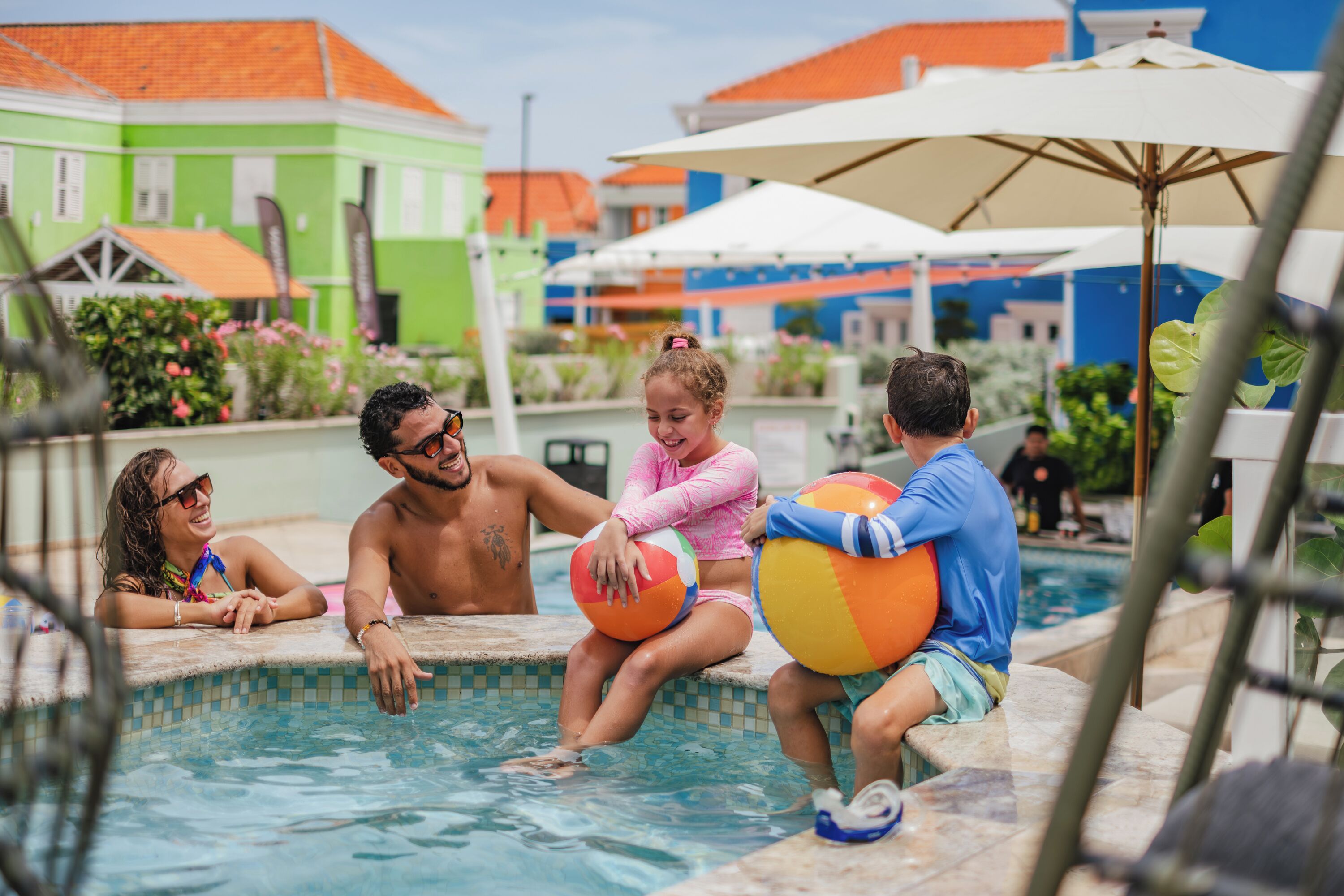 A swimming pool area with people relaxing and holding beach balls.