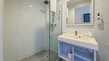 Un baño moderno con ducha de vidrio, un lavabo blanco con espejo y artículos de aseo en la pared.