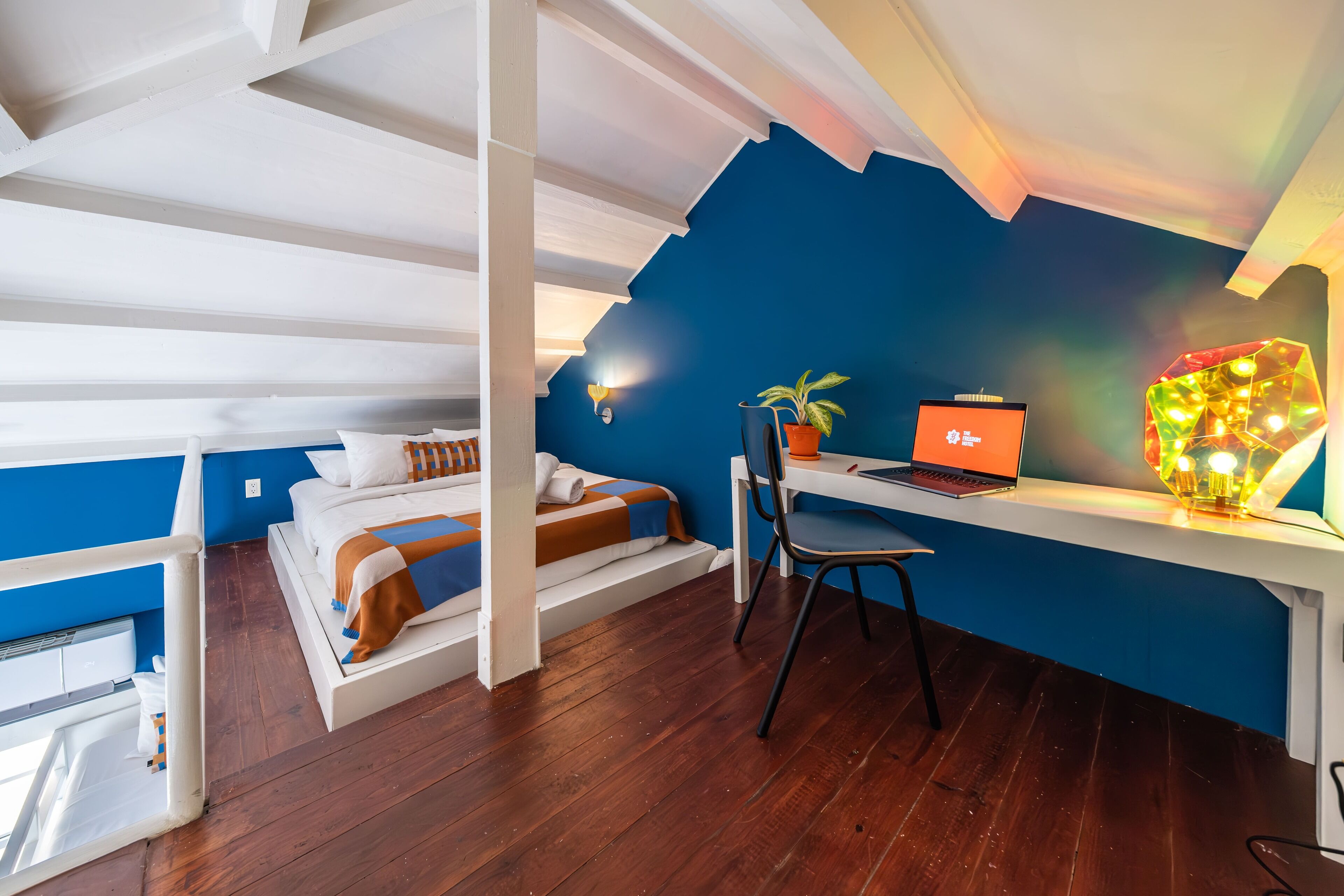 Un dormitorio con cama, escritorio con computadora portátil, silla y lámpara decorativa.