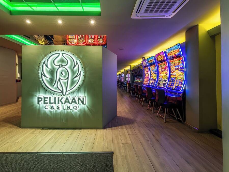Un casino Pelikan con un logotipo destacado, múltiples máquinas tragamonedas y un piso de madera.