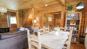 A cozy cabin interior with a wooden dining table, a sofa, and a bookshelf. - Sun View Lodge (Llanbedr)