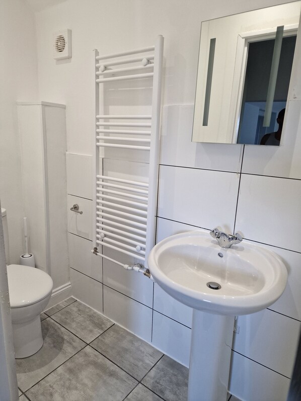 Un baño con inodoro, lavamanos blanco y un perchero para toallas.