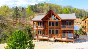 A multi-story wooden cabin with a balcony, surrounded by a forested hillside. - Smokey Mnt. Getaway w/Hot Tub, Deck + Amazing view (Sevierville)