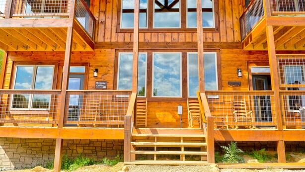 A multi-story wooden building with balconies, large windows, and a stone foundation. - Smokey Mnt. Getaway w/Hot Tub, Deck + Amazing view (Sevierville)