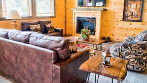 A cozy living room with a leather sofa, patterned armchair, and a fireplace. - Smokey Mnt. Getaway w/Hot Tub, Deck + Amazing view (Sevierville)