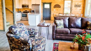 A cozy cabin interior with a kitchen, dining area, and living room furnished with a patterned armchair and a leather sofa. - Smokey Mnt. Getaway w/Hot Tub, Deck + Amazing view (Sevierville)