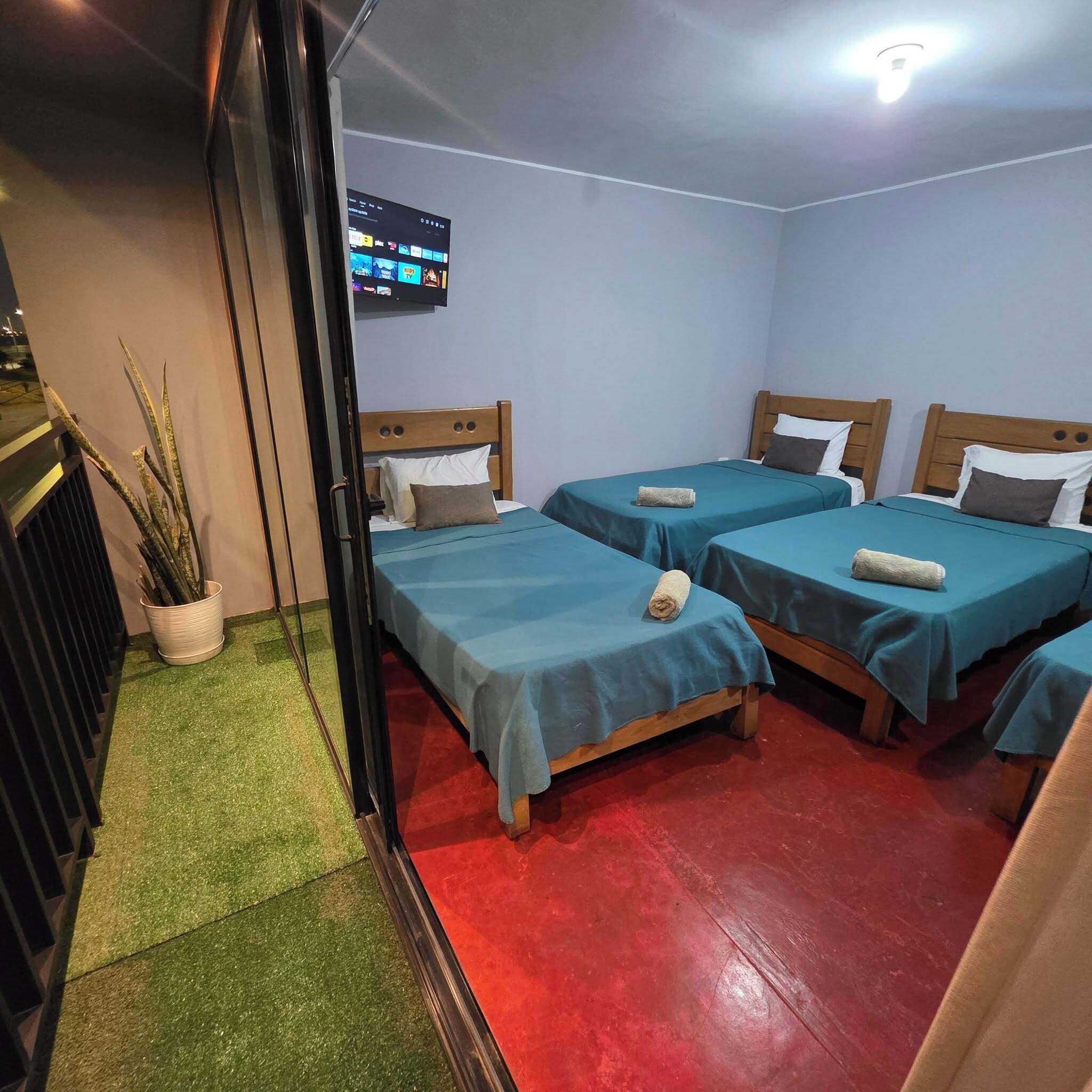 A hotel room with three single beds, a TV mounted on the wall, and a small potted plant.