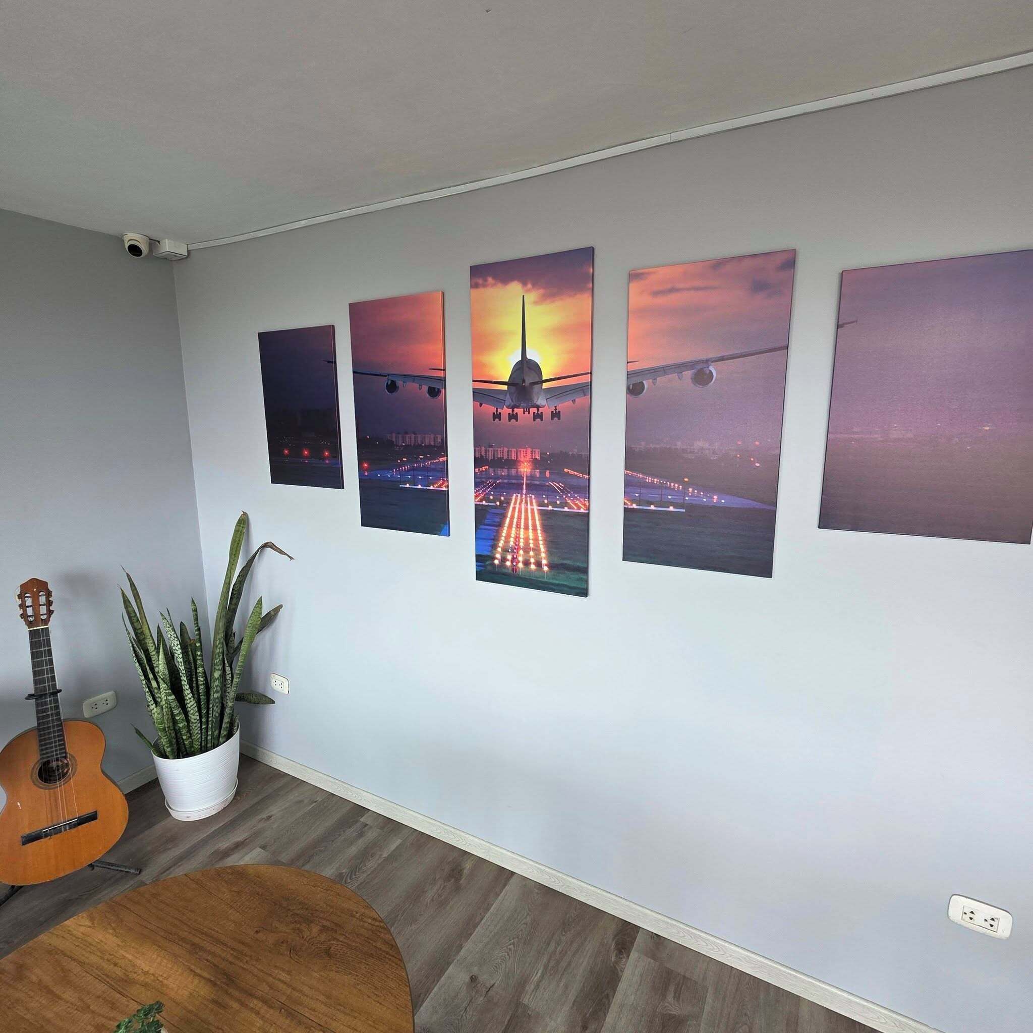 Ein Zimmer mit Holzboden, einer Gitarre, einem Topfpflanzen und vier gerahmten Bildern an der Wand.