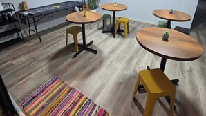 Una habitación moderna con una mesa larga, varias mesas redondas pequeñas y un televisor en la pared.