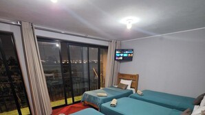 Una habitación de hotel con dos camas, televisión y balcón con vistas a la ciudad.