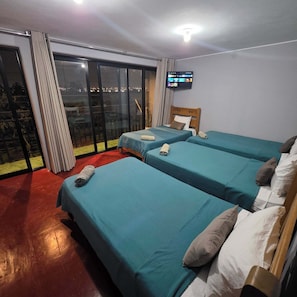 A hotel room with two beds, a TV, and a balcony with a city view. - Lima Airport Hostel (Callao)