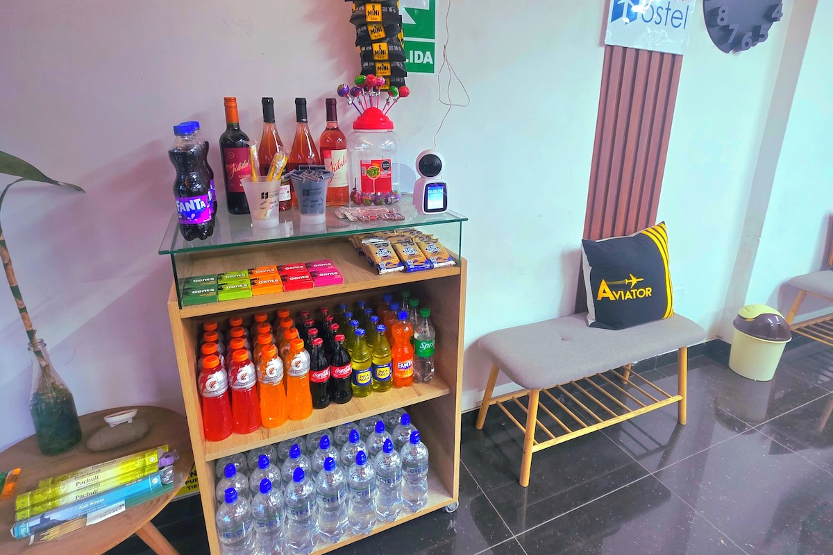 Zona de recepción de hotel con mostrador que exhibe diversas bebidas, un reloj y un cartel que indica la ubicación.
