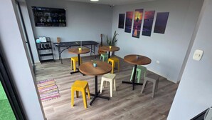 Una habitación moderna con suelo de madera, una mesa negra con sillas, un televisor montado en la pared y un ventanal.