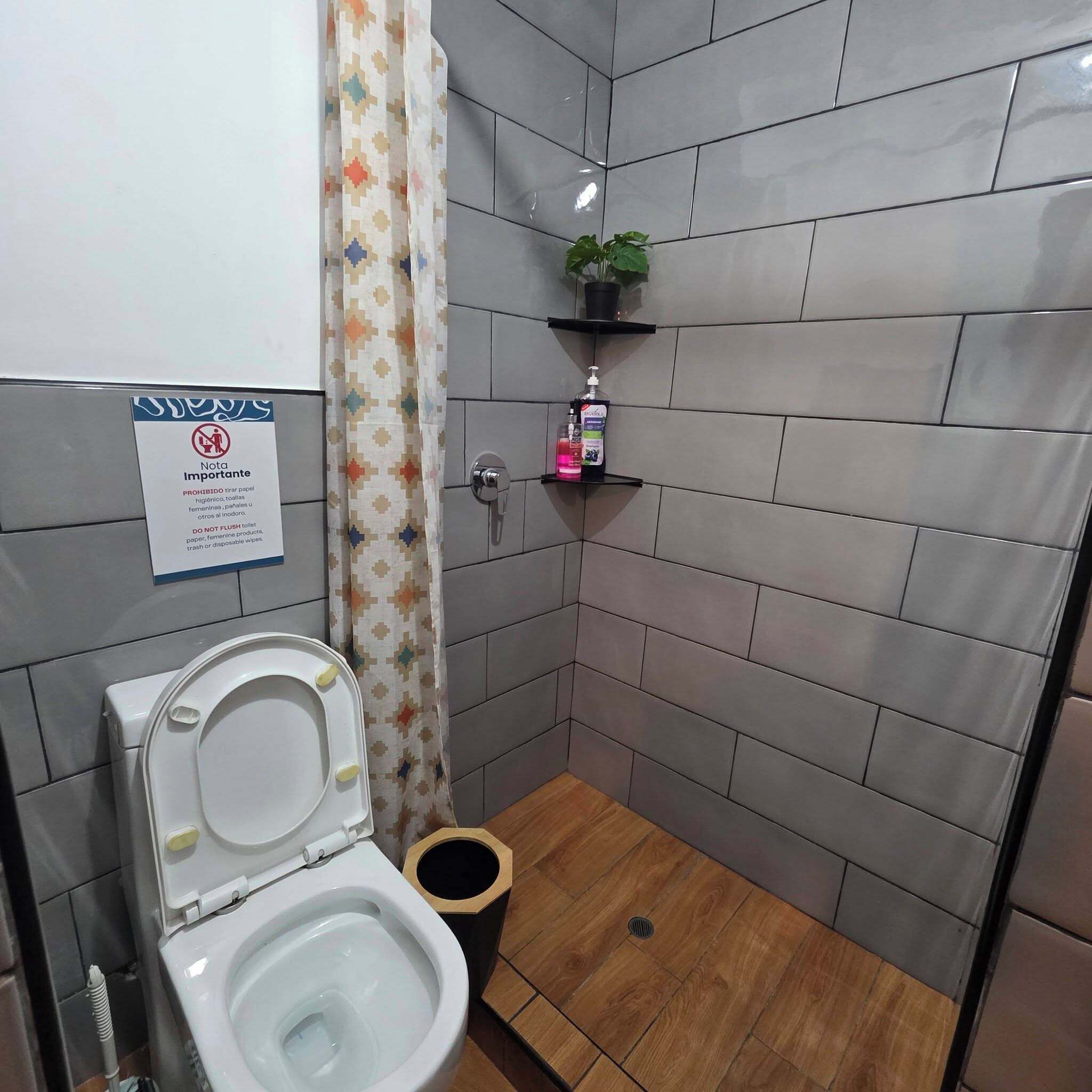 A small bathroom with a toilet, a shower curtain, a shelf with toiletries, and a sign on the wall.