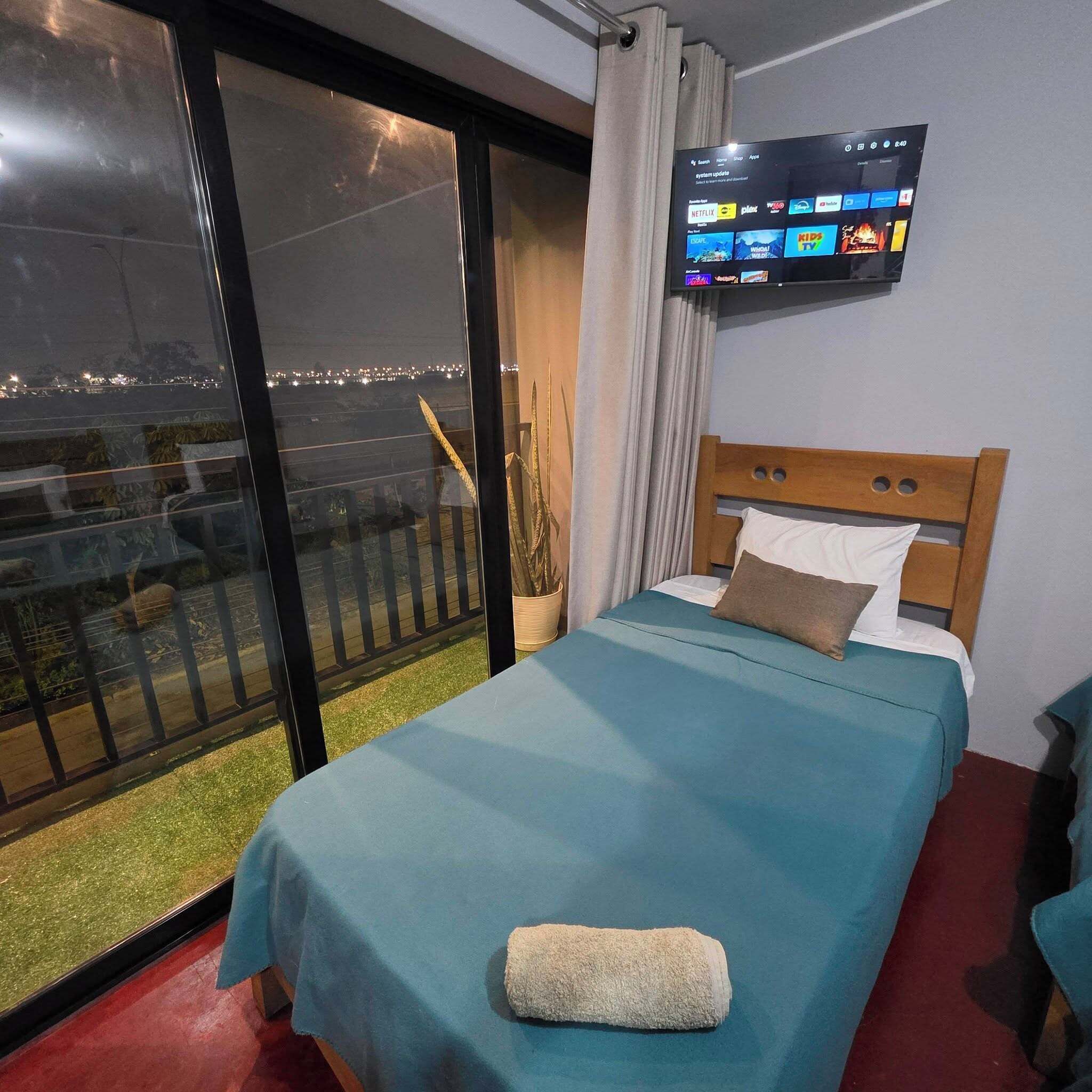Une chambre d’hôtel avec un lit, un téléviseur fixé au mur et un balcon offrant une vue sur la ville la nuit.