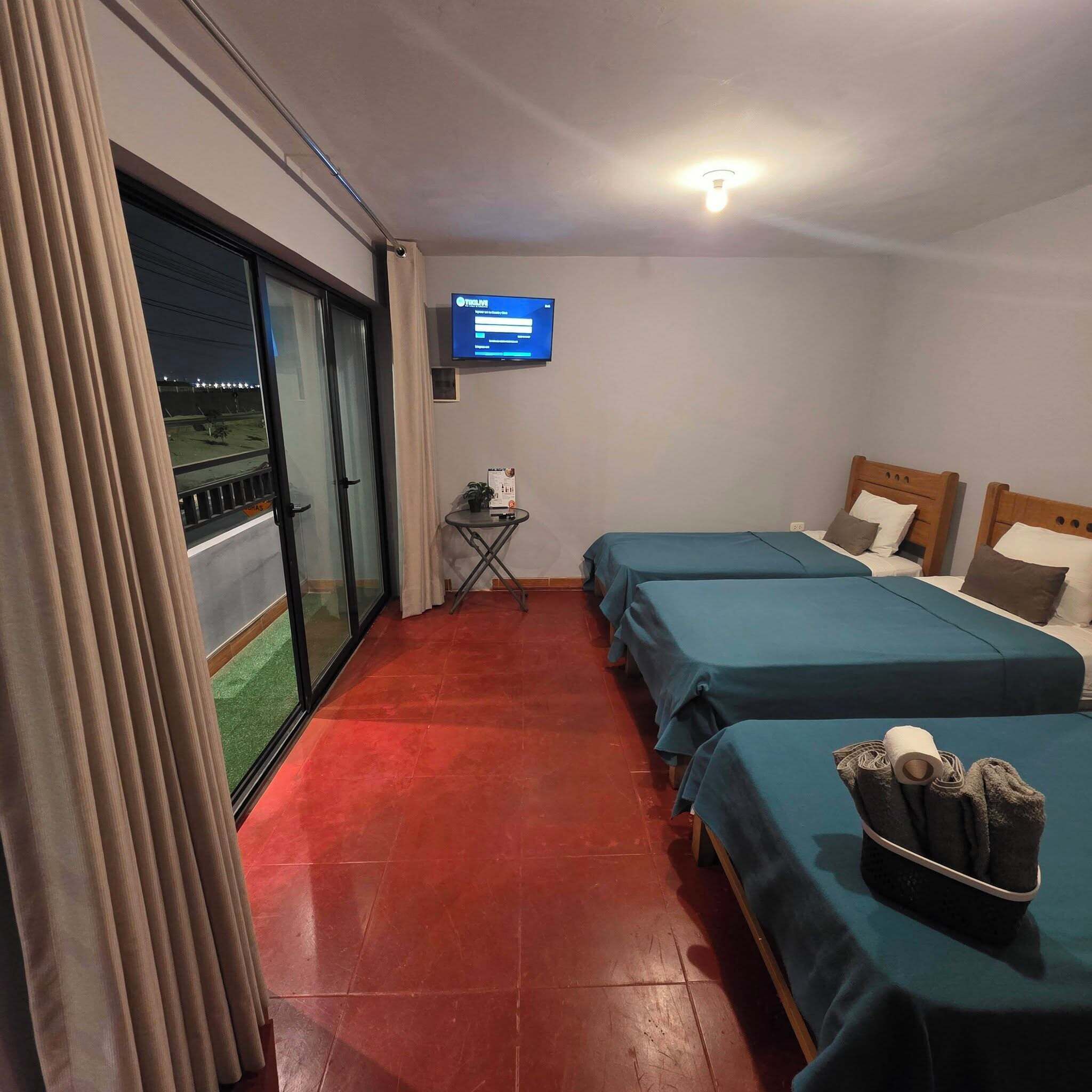 Une chambre d’hôtel avec deux lits, une télévision, une petite table et une vue sur l’extérieur, accessible par une porte coulissante.