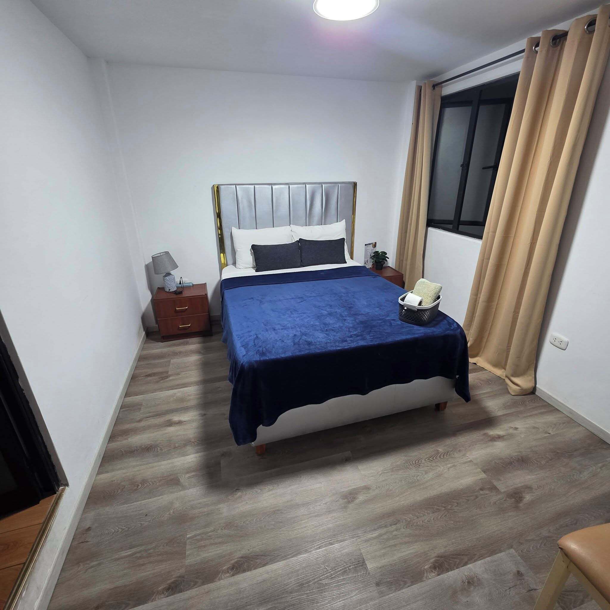 A bedroom with a bed, bedside table, lamp, and a window with curtains.