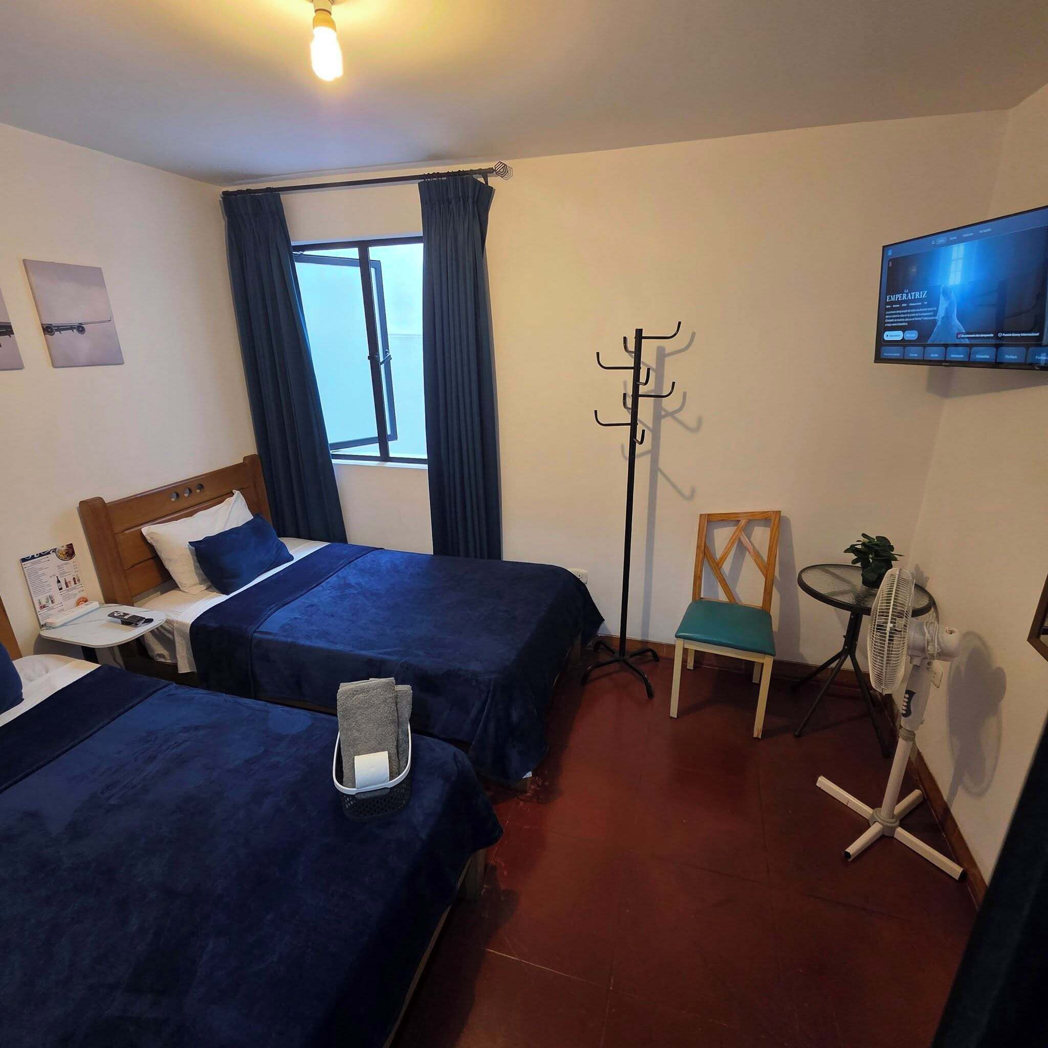 Ein Hotelzimmer mit zwei Betten, einem Fernseher, einem Kleiderständer, einem Stuhl und einem Ventilator.