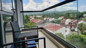 A balcony with a view of a residential area, a chair, and a table. - 24/7 Security, 2B/R Paradise w/Infinity Rooftop Pool & City Views 🌴🏊 (Kingston 10)