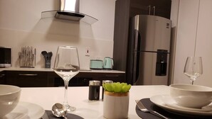 A modern kitchen with a dining table set for two, featuring a minimalist design with a white countertop, stainless steel appliances, and a decorative plant centerpiece. - 24/7 Security, 2B/R Paradise w/Infinity Rooftop Pool & City Views 🌴🏊 (Kingston 10)