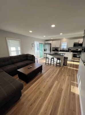 Relax in this stylish living space with a dark brown sofa, wooden coffee table, and modern kitchen area.